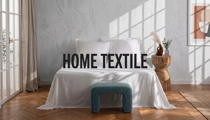 A styled bedroom scene with a bed dressed in white bedding, a teal upholstered bench at the foot, a wooden side table with dried stems, and large overlaid text reading “HOME TEXTILE.”.